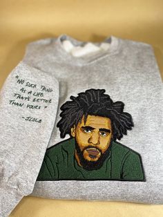 "Wrap yourself in comfort and style with this custom embroidered sweatshirt featuring a detailed portrait of the legendary rapper J. Cole on the chest, and his iconic lyric \"No such thing as a life that's better than yours\" stitched on the right sleeve. The sweatshirt's design captures the essence of J. Cole's artistry and delivers a powerful message of self-worth and positivity. 🎨 **Customization Options You have the freedom to choose the color of J. Cole's shirt on the portrait as well as t J Cole Sweatshirt, Custom Embroidered Sweater For Fall Streetwear, Custom Embroidery Sweater For Fall Streetwear, Fall Custom Embroidered Sweater For Streetwear, Winter Sweater With Custom Embroidery For Streetwear, J Cole Hoodie, J Cole T Shirt, Cozy Love, Detailed Portrait