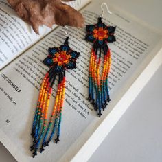 a pair of colorful beaded earrings sitting on top of an open book next to a leaf