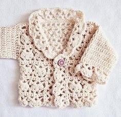 a crocheted sweater with buttons on the collar and sleeves is laying on a white surface