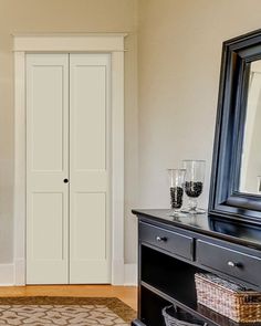 a room with a dresser, mirror and two wine glasses on the table in front of it