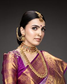 a woman in a purple and gold saree with jewelry on her neck, wearing an elaborate