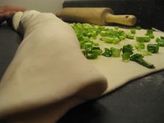 chopped green vegetables are being prepared on a cutting board with a rolling pin in the background