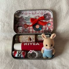 an open tin with some items in it on a white tablecloth and a red bow