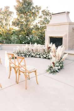 an outdoor wedding setup with chairs and flowers on the table, in front of a fireplace