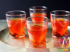 four glasses filled with liquid sitting on top of a metal tray next to each other