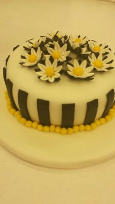 a white and black striped cake with daisies on the top is sitting on a table