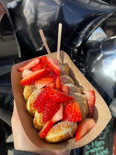 strawberries and powdered sugar on top of pastries in a paper container with toothpicks