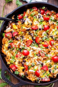 a skillet filled with taco salad on top of a wooden table next to tomatoes and cilantro