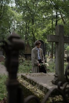 a man standing in front of a cemetery with a cross on the ground next to it