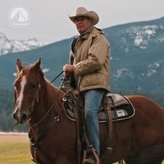 a man riding on the back of a brown horse in a field next to mountains