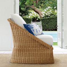 a wicker chair with blue and white pillows on it in front of an open door