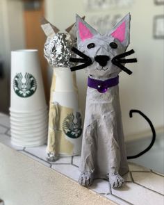 a paper mache cat sitting on top of a counter next to two starbucks cups