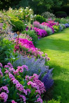 a garden filled with lots of purple flowers and green grass next to a lush green field