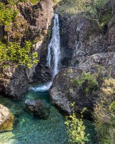 a small waterfall in the middle of some rocks and green plants on either side of it