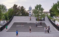 many people are walking up and down the stairs in front of some buildings with trees