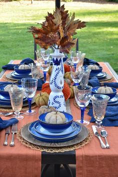 the table is set with blue and white plates, silverware, and pumpkins