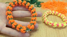 someone is holding two different bracelets on their fingers, one has an orange and green braid