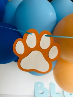 an orange and white paw print hangs from a string next to blue and yellow balloons