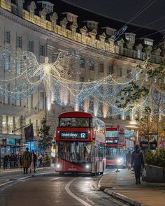 a double decker bus driving down a street next to tall buildings with christmas lights on them