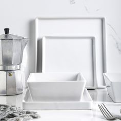 a white table topped with plates and silverware next to a coffee pot on top of a counter