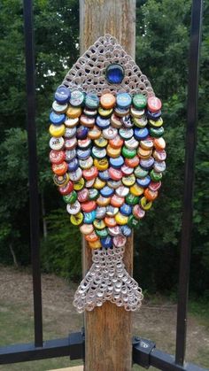 a wooden pole with many bottle caps hanging from it's sides and a tree in the background