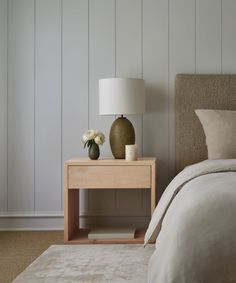 a nightstand with two vases on top of it next to a bed and lamp