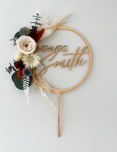 a cake topper with flowers and feathers in the shape of a circle that says,'mrs south '