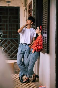 two people leaning against the side of a building and one person is holding something in his mouth