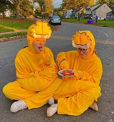 two people dressed in costumes sitting on the ground eating food from a plate with their mouths open