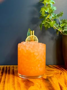 a tall glass with an orange drink in it on a table next to a potted plant