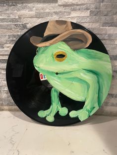 a green frog with a hat sitting on top of a black plate