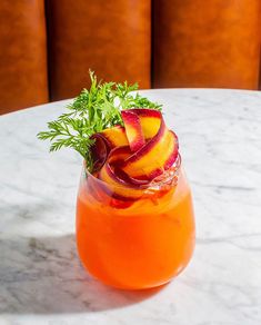 an orange drink with sliced peaches and parsley in a glass on a marble table