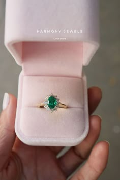 a close up of a person's hand holding a ring with a green stone