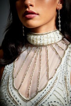 a woman in a white dress with silver beads on her neck and necklaces around her neck