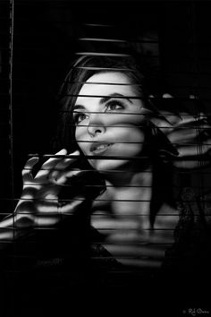 a black and white photo of a woman behind blinds