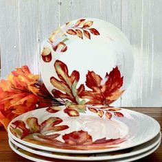 plates with autumn leaves painted on them sit next to an orange and yellow leaf arrangement