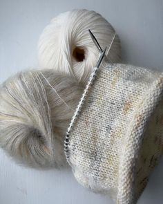 two skeins of white yarn next to a ball of knitting needles on a white surface