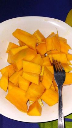 a white plate topped with cut up mangoes and a fork on top of it