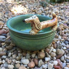 a dog figurine sitting in a bowl filled with rocks and gravel on the ground