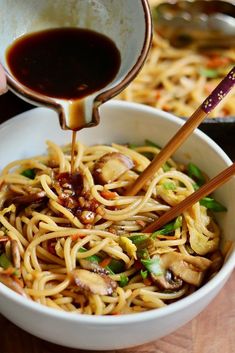 someone pouring sauce over noodles in a white bowl with chopsticks and green onions