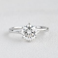 a white gold engagement ring with a round brilliant cut diamond in the center, on a plain surface