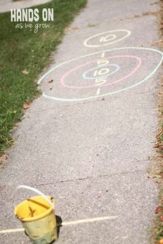 a yellow bucket sitting on the side of a sidewalk next to a chalk drawing circle