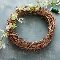 a grapevine wreath with green leaves and purple flowers