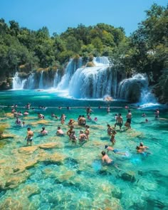 many people are swimming in the blue water near a large waterfall and some green trees