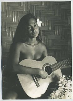 an old photo of a woman holding a guitar and posing for the camera with flowers in her hair