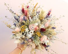 a bouquet of flowers is being held up by someone's hand in front of a pink wall