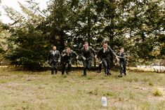 a group of men in suits and ties running through the grass with trees behind them