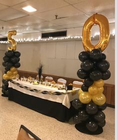 a table topped with black and gold balloons next to a white table cloth covered table