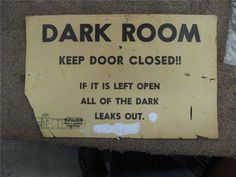 a sign that is on the floor in front of a door saying, dark room keep door closed if it is left open all of the park leaks out