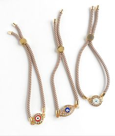 "Beautiful pave evil eye bracelets with a champagne color Milan Rope closure. Closure is adjustable and convenient. ✨Fun Fact✨ The evil eye, known as \"mati\" (μάτι) in Greek culture, is a curse thought to be given by a malicious glare that can cause bad luck or loss. That's why it's important to wear an evil eye somewhere on your body to ward off this curse and protect yourself throughout the day. 👀 So, this HeartString Evil Eye bracelet not only is chic and beautiful, but possibly help you wa Adjustable Beige Jewelry With Sliding Knot, Adjustable Gold Evil Eye Bracelet For Everyday, Adjustable Beige Jewelry, Adjustable Length Beige Jewelry, Beige Jewelry With Adjustable Length For Gift, Beige Jewelry Gift With Sliding Knot, Adjustable Round Beige Bracelets, Adjustable Beige Bracelets, Beige Adjustable Length Jewelry For Gift